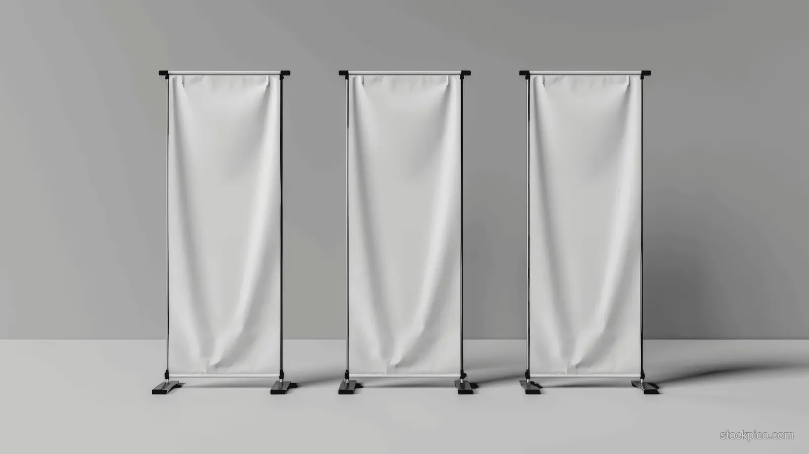 Three empty white roll-up banner stands stand in a row on a grey studio background.