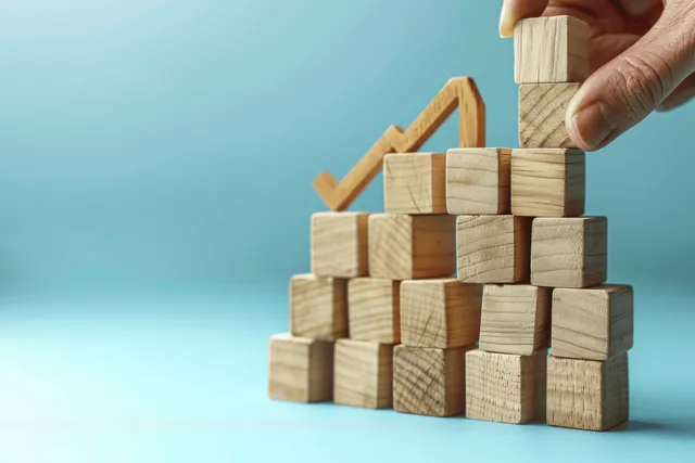 A hand stacks wooden blocks as an up arrow indicates rising interest rates and finance growth.