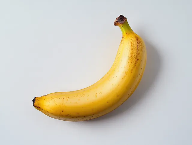 A single ripe yellow banana with small brown spots isolated on a plain white background.