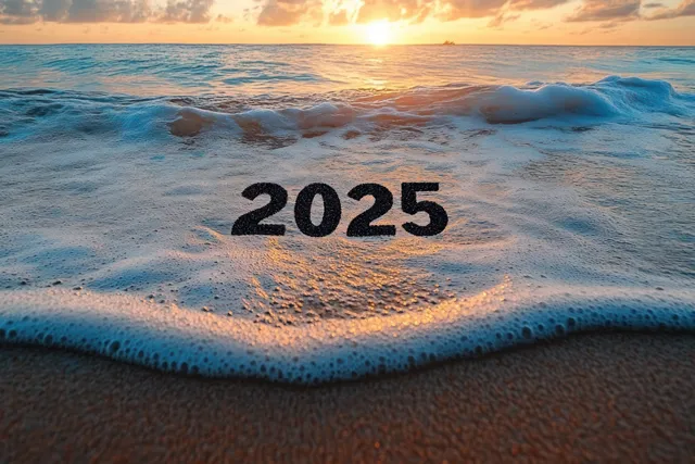 “2025” is written in wet beach sand as ocean waves roll in at sunset.