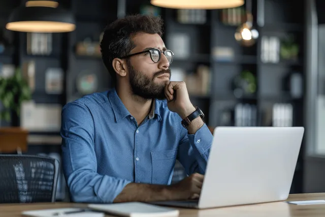Focused young businessman in blue shirt typing on laptop at office desk