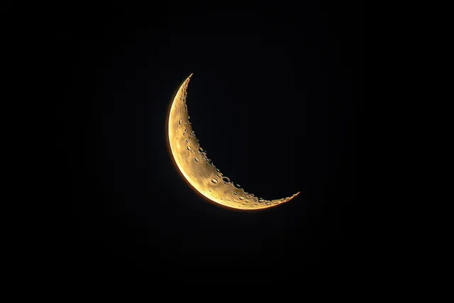A glowing crescent moon with visible craters against a dark night sky.