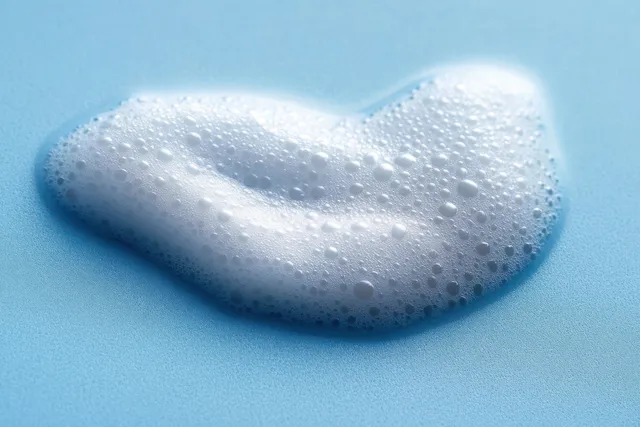 Heart-shaped foam cleanser with tiny bubbles on a blue background for facial cleaning.