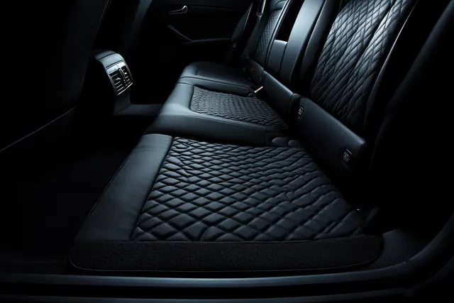 Dark luxury car cabin showing quilted black leather rear seats with detailed stitching and seat controls.