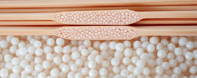 Close-up of smooth white wax beads for depilation with a wooden stick on a pink minimal background.