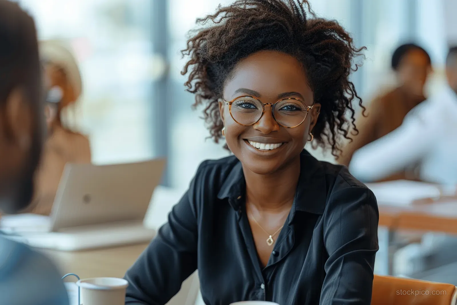 African American businesswoman sits at a conference table leading a team discussion with colleagues in an office.