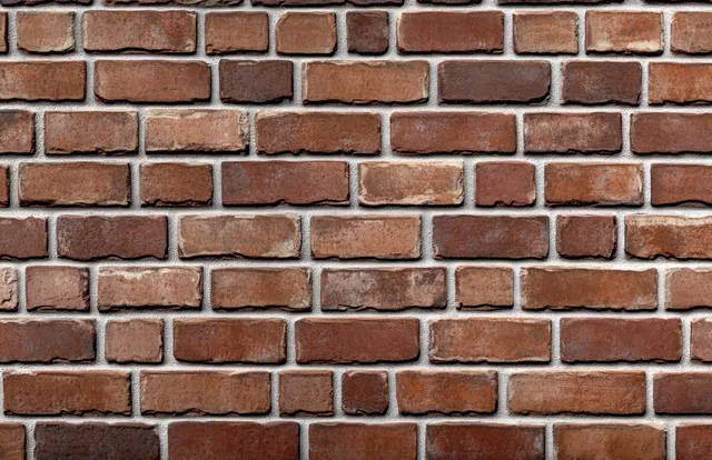 Close-up of a weathered brick wall with red and brown bricks arranged in a staggered pattern and visible mortar.