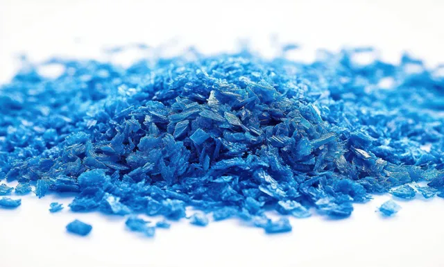 Close-up of a pile of shiny blue flakes scattered on a white surface with metallic sparkle.