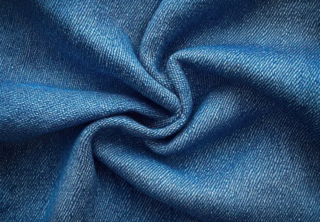 Twisted blue denim fabric close-up shows detailed woven threads and diagonal weave patterns.