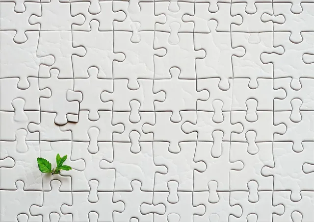 A mostly completed white jigsaw puzzle has one missing piece, showing a green sprout through the gap.