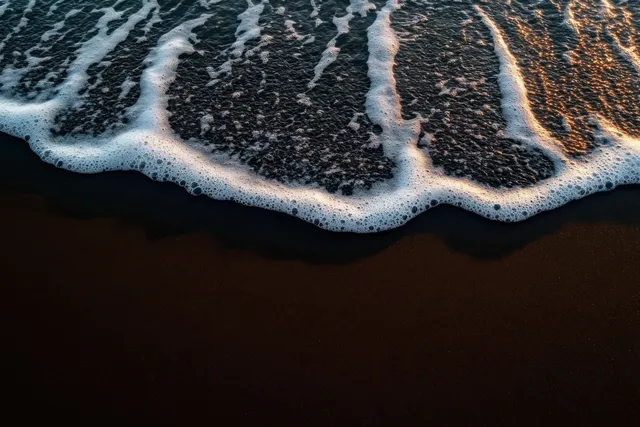 Aerial beach shoreline with gentle waves, foamy surf, golden-hour sky glow
