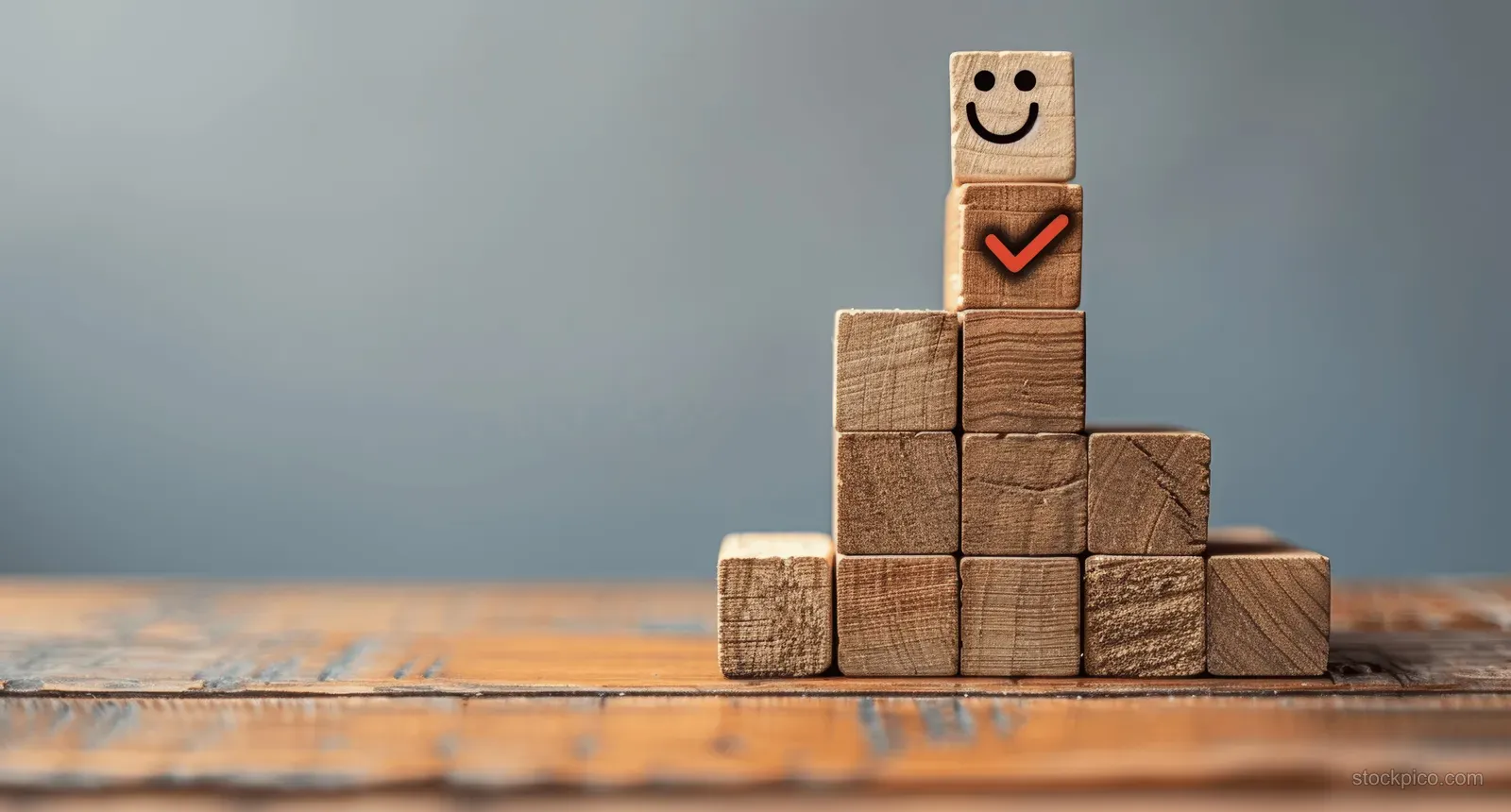 Wooden blocks stacked on stairs display a checkmark and smiling face against a neutral background.