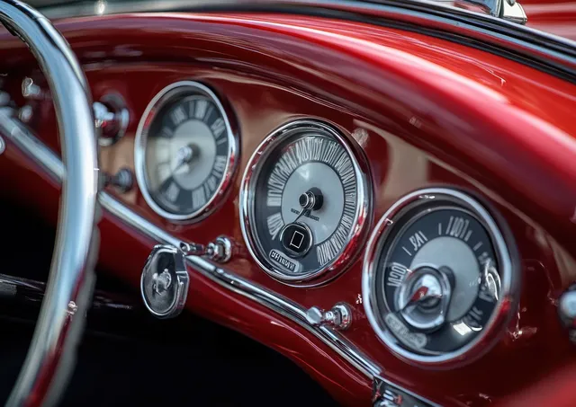 Shiny red vintage car dashboard with chrome round gauges and analog speedometer dials.