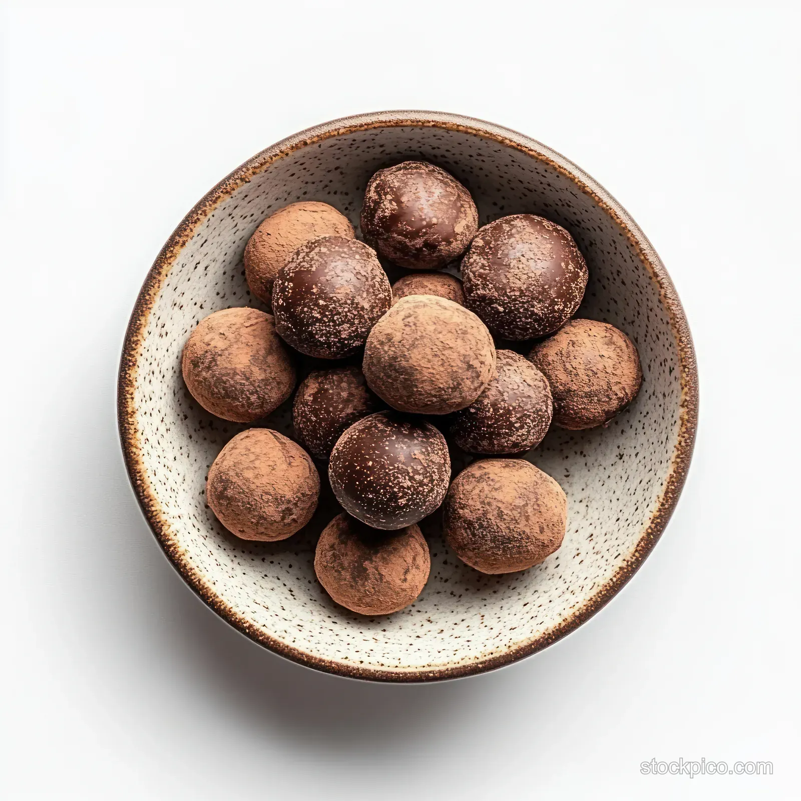 Chocolate truffles piled in a speckled ceramic bowl with soft shadows on a white background.