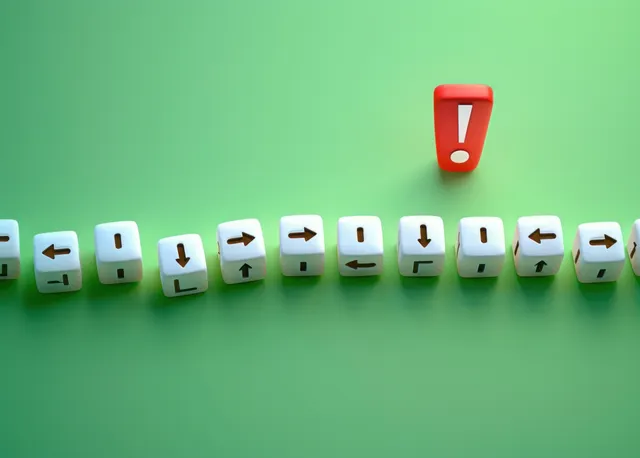 A line of white cubes with arrow symbols lies on green ground while a single red cube with an exclamation mark stands upright.