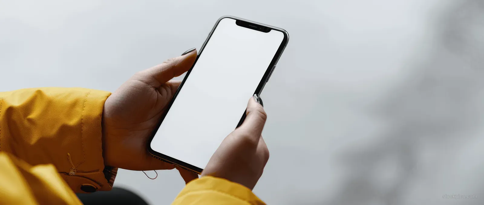 Close-up of a woman’s hands holding a smartphone with a blank screen against a light background.