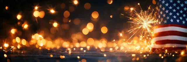 American flag with fireworks bursting at night, golden bokeh lights along the horizon