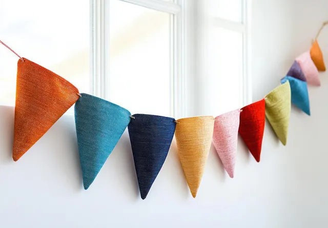 Colorful fabric bunting flags strung across an indoor wall by a bright window