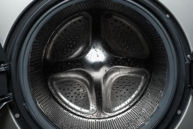 Water droplets cling to the shiny metal interior of a front-loading washing machine drum.