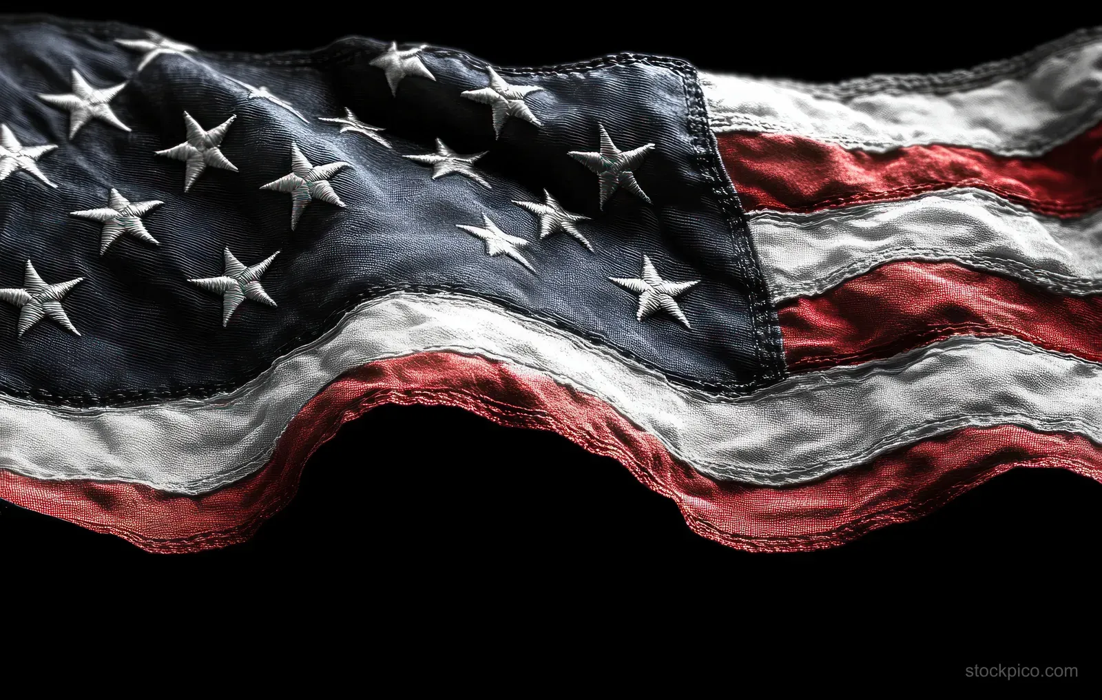 Worn American flag waves in close-up, showing blue stars and red-and-white stripes against a black background.