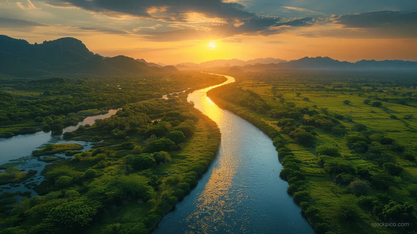 Aerial view of a winding river delta with green meadows and mountains under a sunset sky.