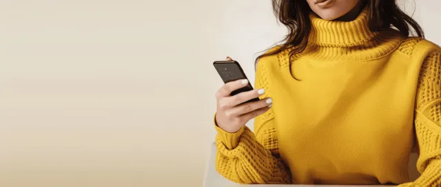 Young woman in yellow sweater using smartphone in office, close-up hand typing message