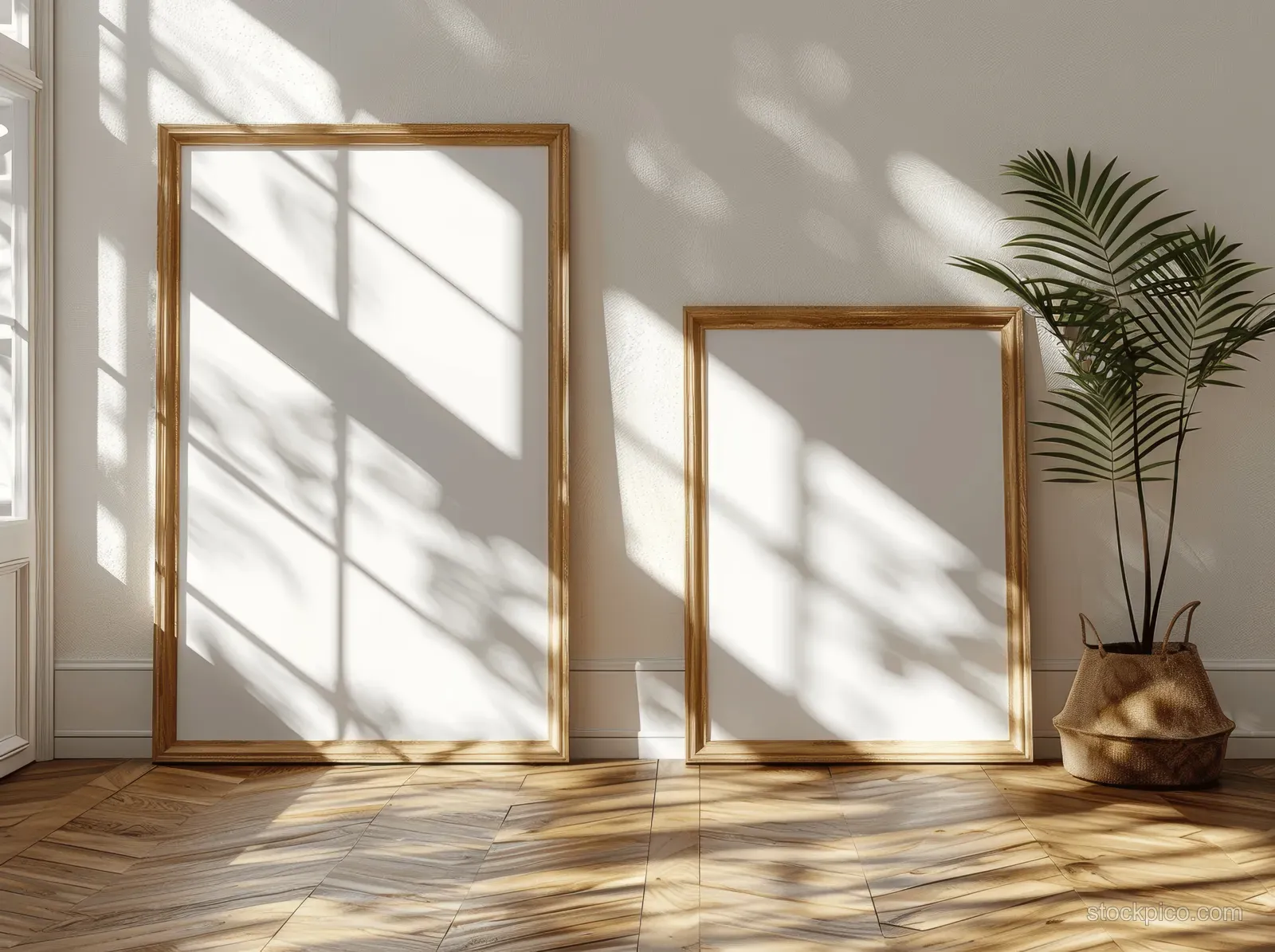 Two wooden picture frames lean in a bright room, with sun shadows cast across the parquet floor and wall.