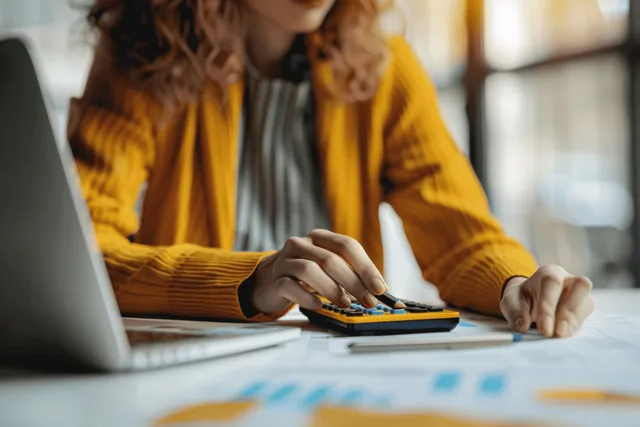 Businesswoman calculating finances with calculator beside laptop and growth chart on office desk
