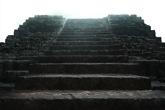 Steep ancient stone steps fade into fog while light glows at the top of a ruined stone structure.