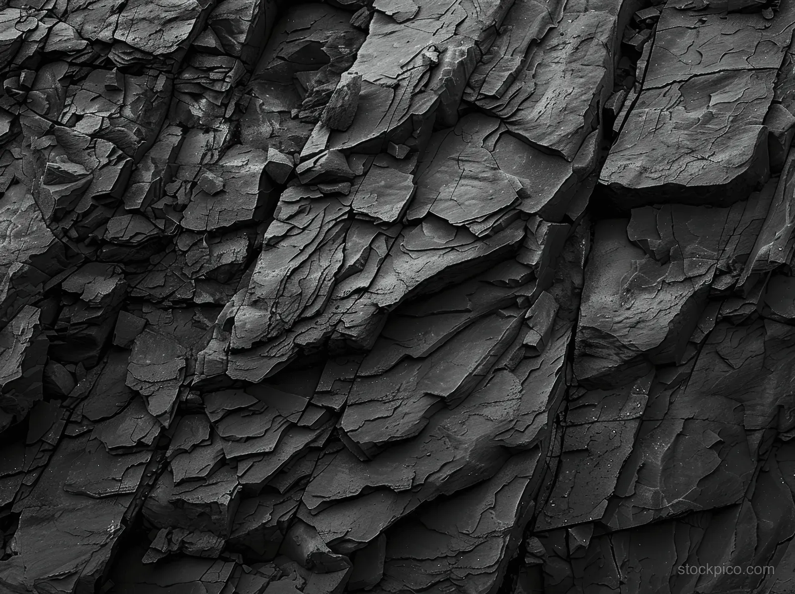 Close-up of a black and white cracked rock cliff wall with layered stone plates and dark fissures.