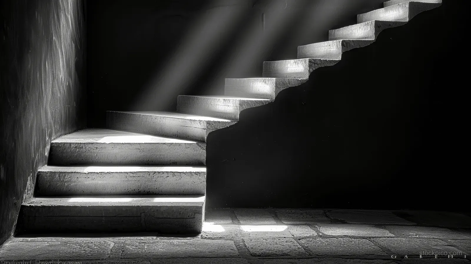 A dark interior staircase rises while window light casts long shadows across gray stone steps.