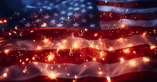 Sparklers flare across a close-up American flag, illuminating the stars and stripes during a July 4 celebration.