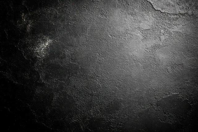 Close-up of a dark rough concrete wall with uneven weathered patches and shadowy texture detail.