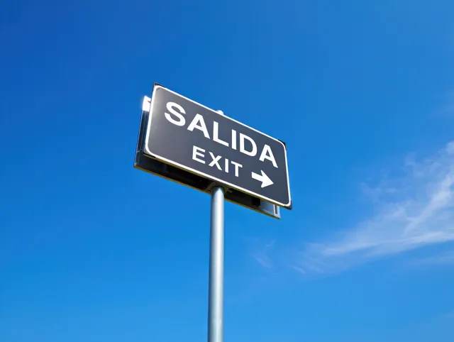 Bilingual EXIT road sign with arrow pointing right against bright blue sky