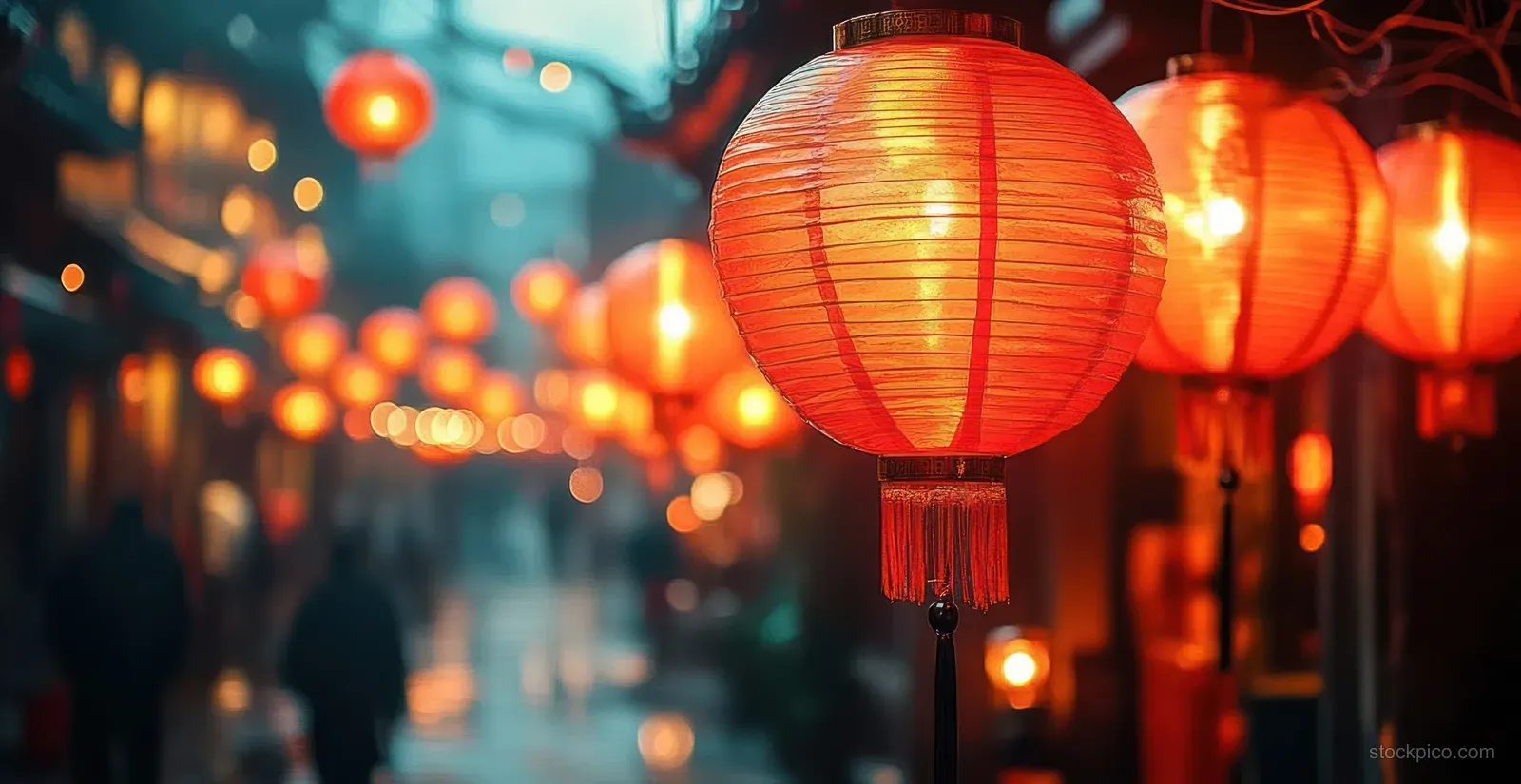 Red Chinese New Year lanterns hang along a blurred night street with warm bokeh lights behind them.