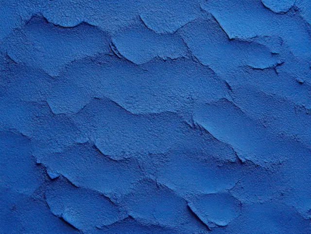 Close-up of a blue wall with peeling and cracked paint exposing uneven layers beneath.