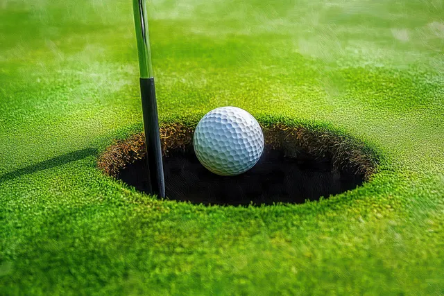 Golf ball poised on the lip of a hole beside a bright flagstick in green grass