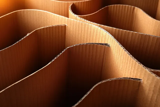 Layered corrugated cardboard sheets with wavy edges and ridged texture under warm light.