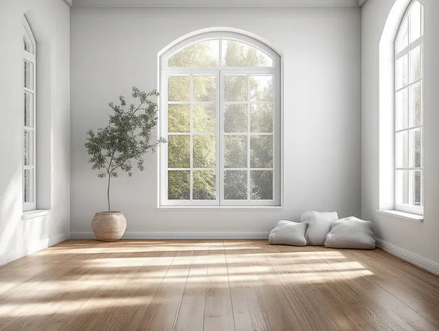 Sunlit Scandinavian minimalist room with a large arched window, light wood floor, and resting cushions.