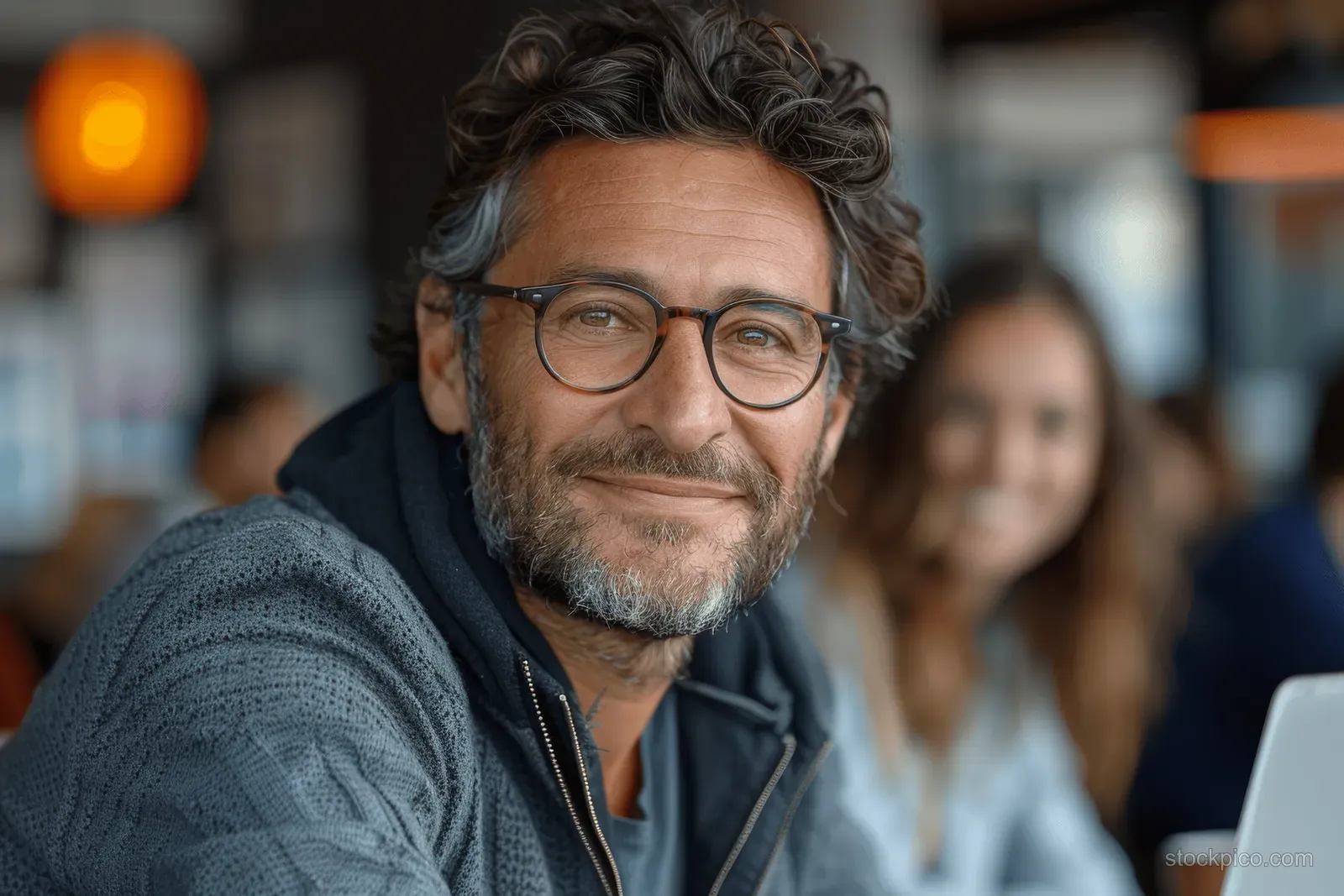 Smiling businessman with glasses works on a laptop at an office table with a female colleague.