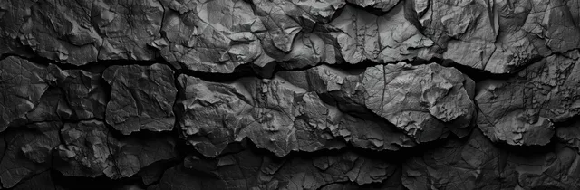 Panoramic monochrome wall of fractured volcanic rock with deep cracks and dark cave-like shadows.