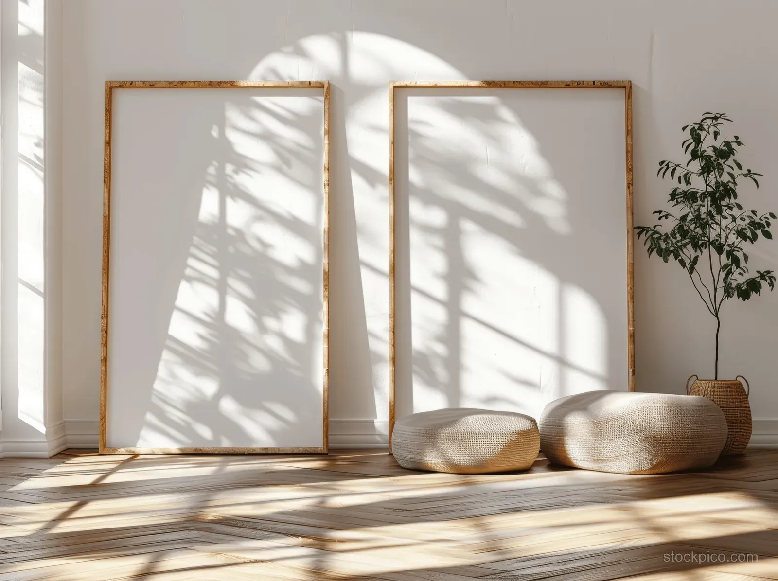 Two blank wooden frames lean on a white wall while window shadows stretch across a parquet floor.