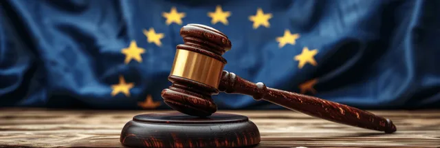 A wooden gavel sits on a table with the European Union flag draped behind it.