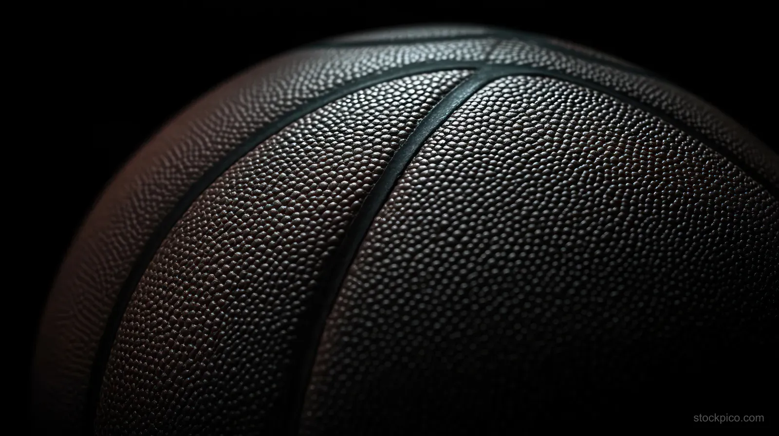 Close-up of a basketball showing pebbled grip texture and dark grooves under focused lighting.