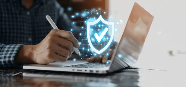 Businessman typing on laptop while a glowing digital shield secures data in office