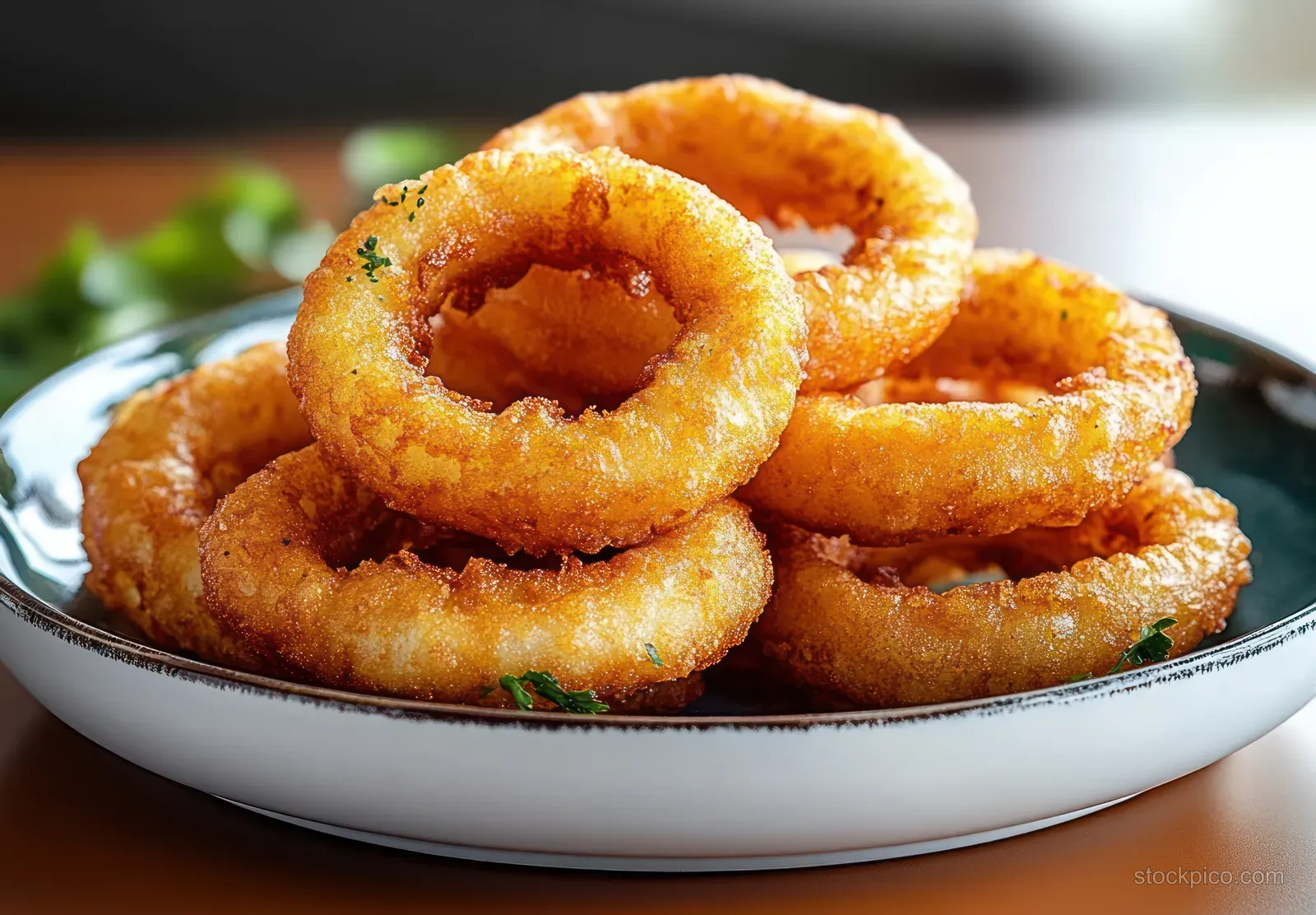 Stacked golden crispy onion rings on a white plate with small green herb garnish.