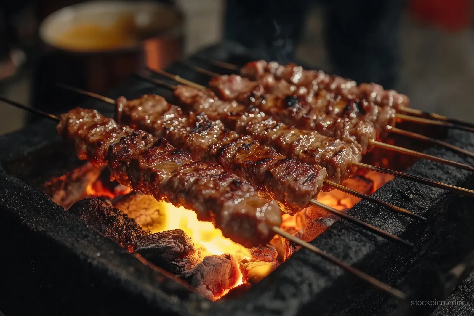 Chicken satay skewers grill over charcoal with visible flames and a smoky caramelized marinade.