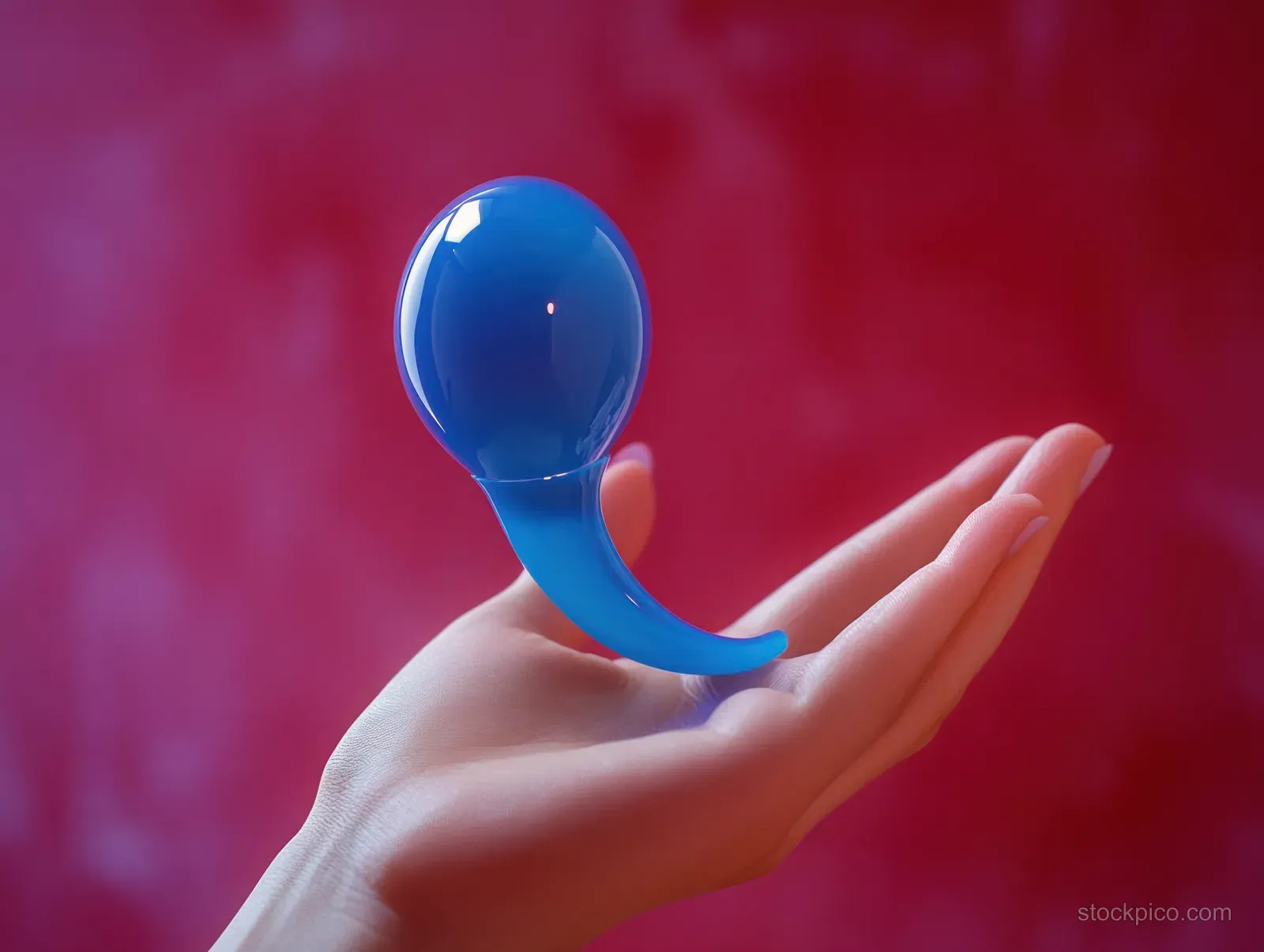 A hand holds a glossy translucent blue teardrop object against a blurred red background.