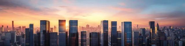 Panoramic skyline at sunset with reflective glass skyscrapers and a warm orange-blue gradient sky.