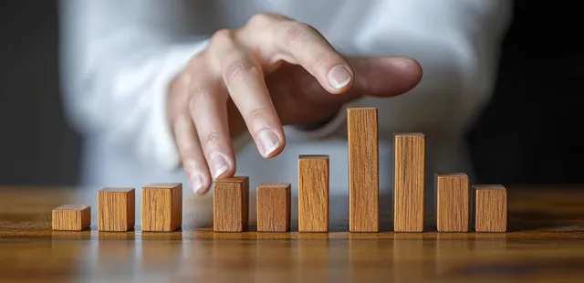Hand stopping falling wooden domino blocks to symbolize risk control strategy